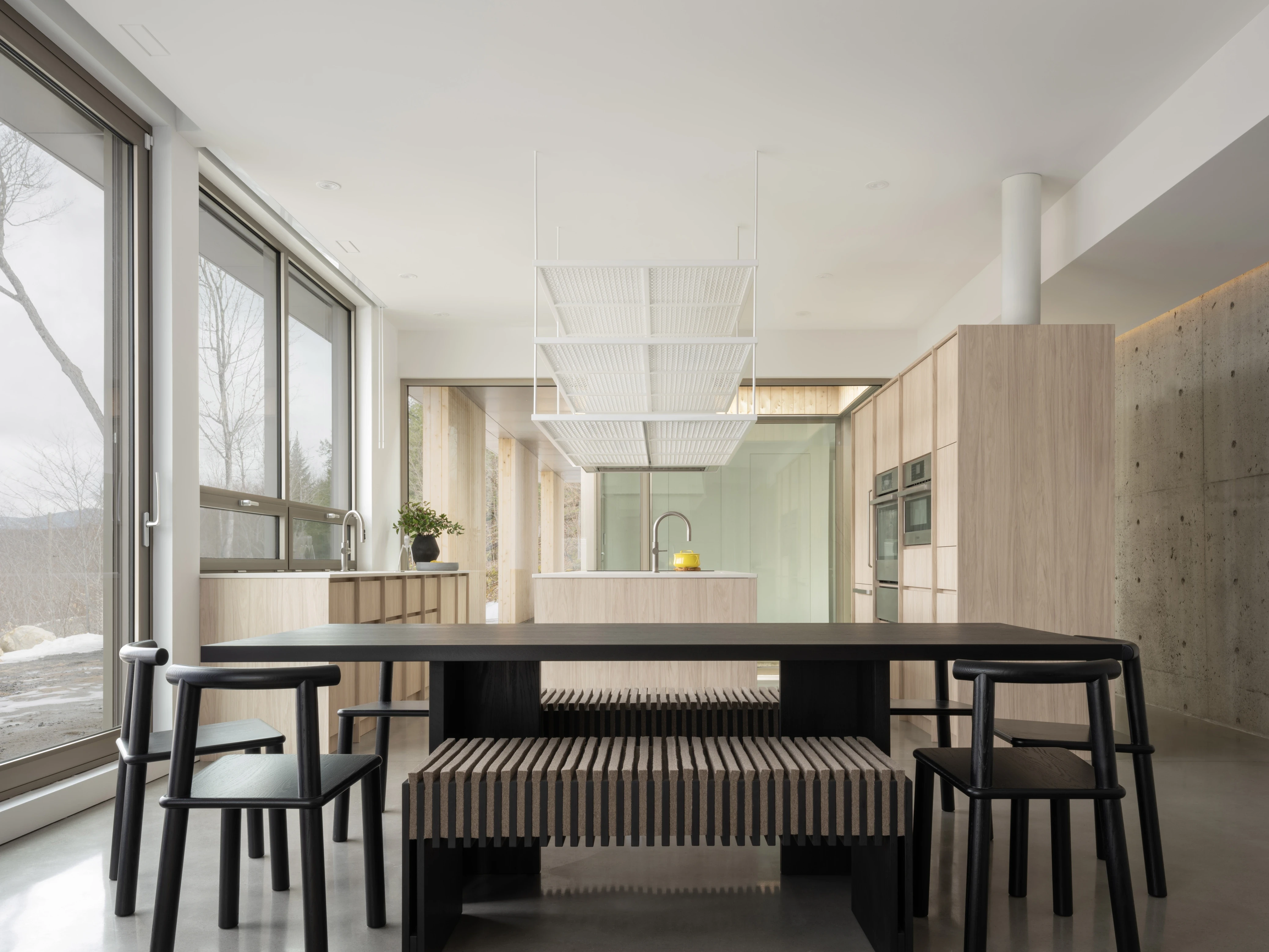 Modern dining area with a large table, minimalist decor, and large windows letting in natural light.