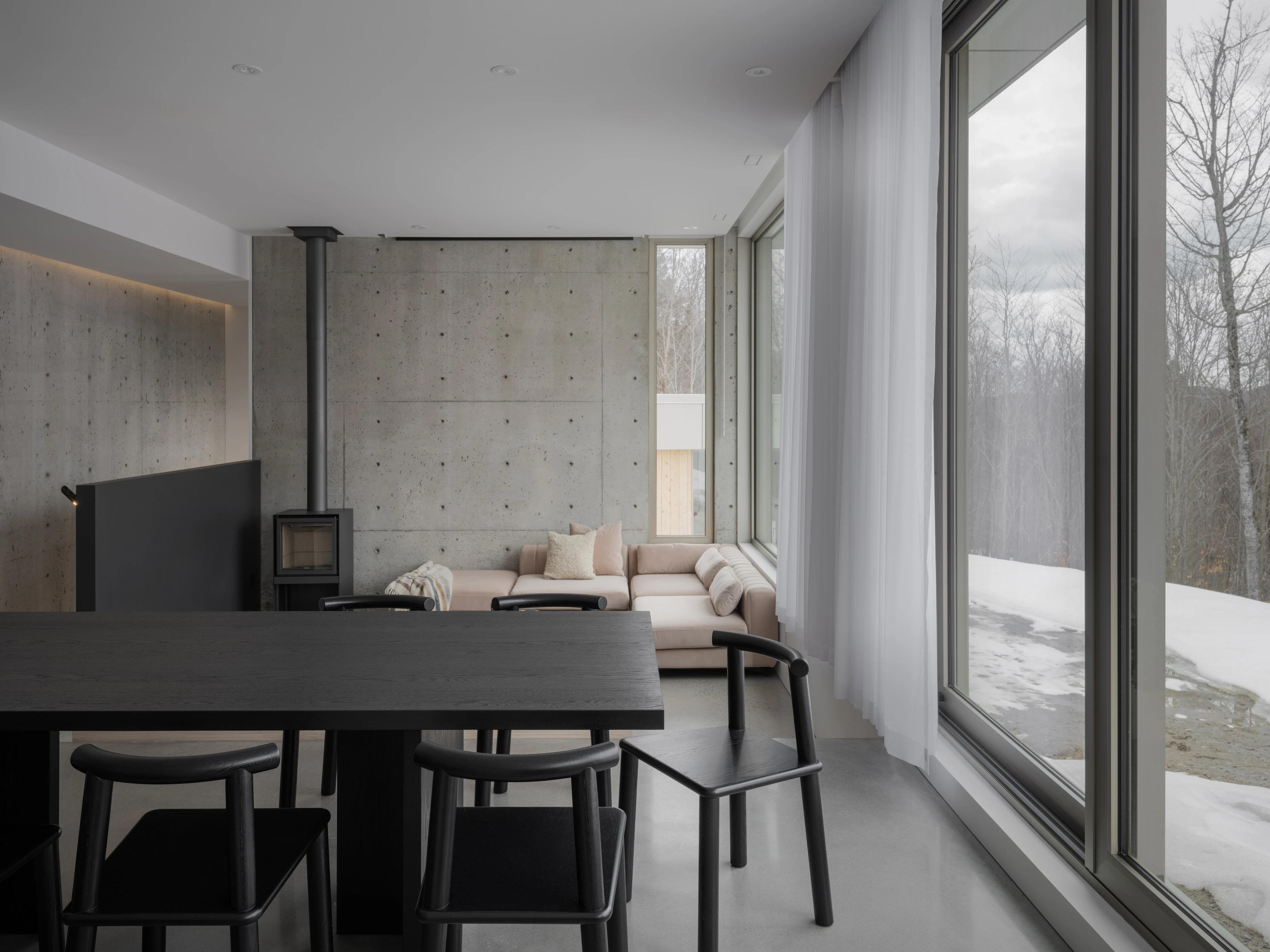 A modern interior featuring a dining area with a black table and chairs, large windows, and minimalistic decor.
