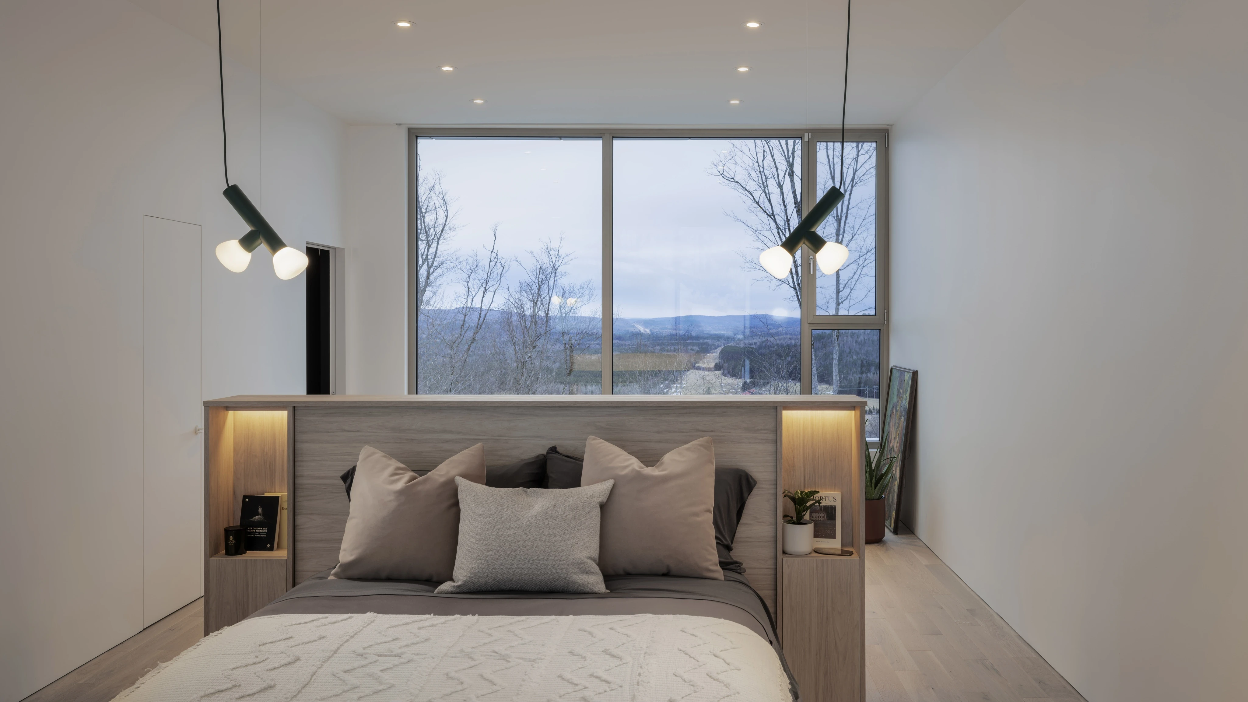 Chambre minimaliste avec lit intégré, éclairage encastré et large fenêtre offrant une vue sur le paysage hivernal.
